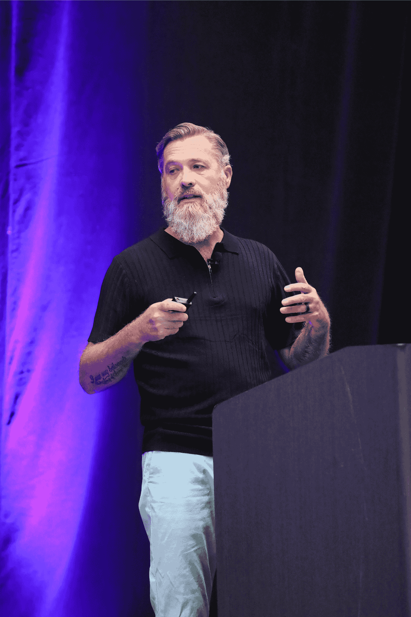 Alan Darsey from Clearwave Fiber presenting on stage at the IQGeo Americas Meetup 2025 in Dallas, addressing a full audience under purple stage lighting