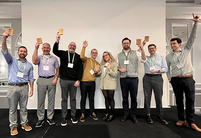 A group of people stand on a stage holding up small award plaques, celebrating together at an event